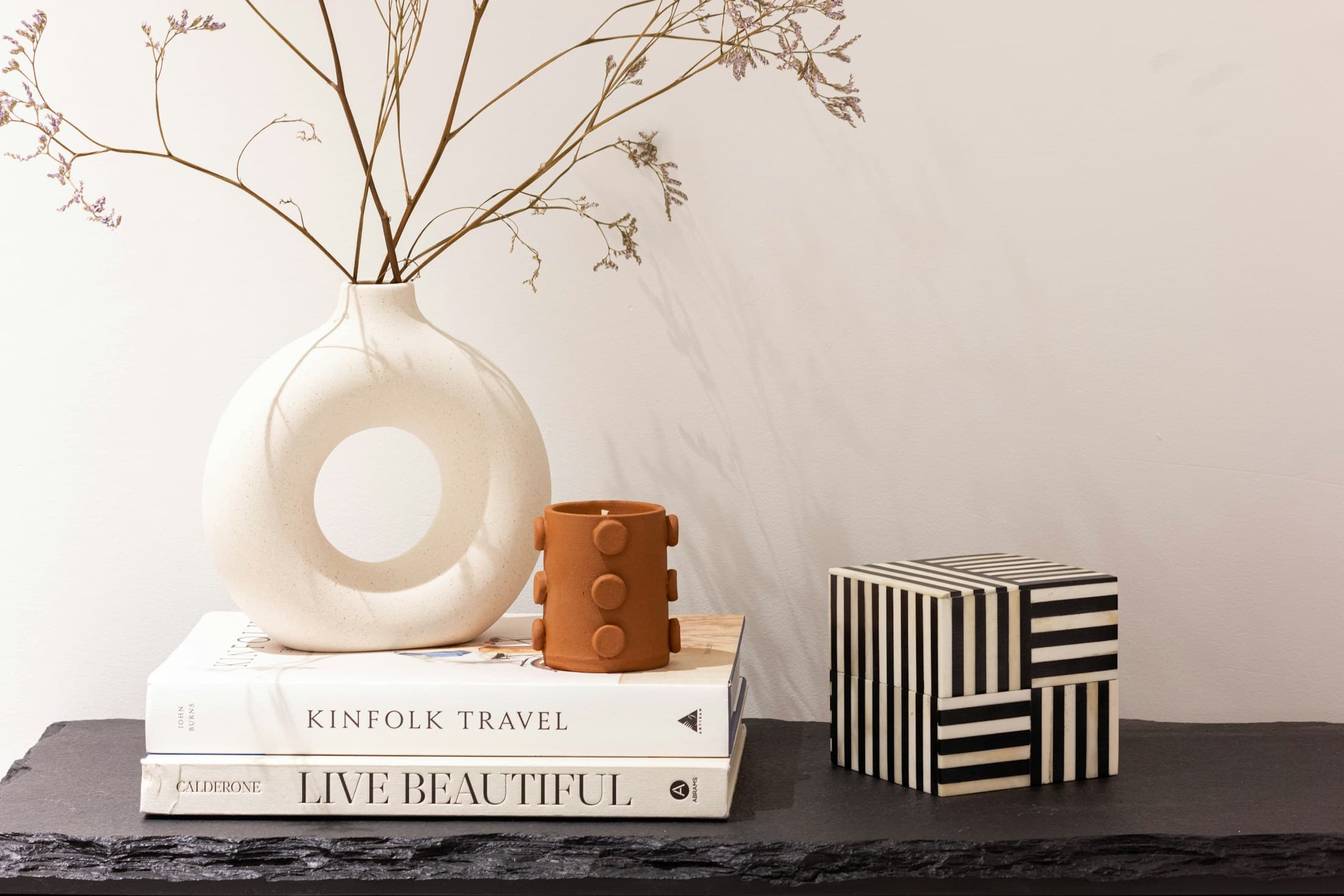 A styled shelf with a ceramic vessel, books, dried stems, and a small accent box.