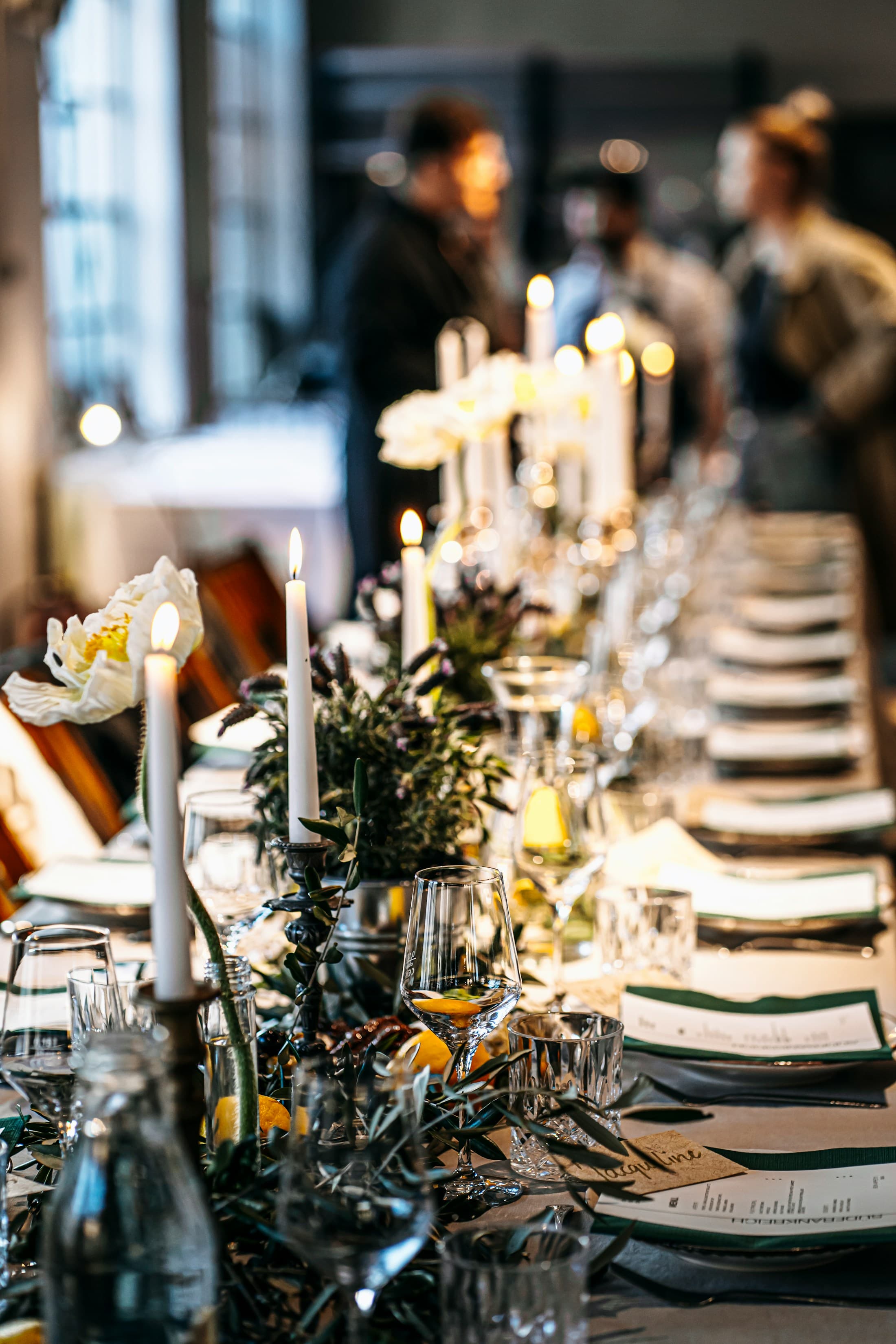 A candlelit table with glassware, flowers, and layered textiles.